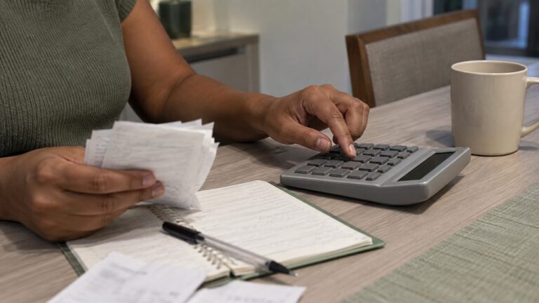 Mãos com calculadora, comprovantes de despesas e caderno de anotações na mesa de casa, no cálculo da pensão alimentícia